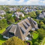 Dorf mit strohgedeckten Häusern und grünen Gärten unter blauem Himmel.
