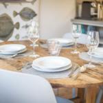 Runder Holztisch mit Tischdecken und Geschirr. Wandbild mit Fischen im Hintergrund.