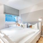 Schlafzimmer mit weißem Bett, Fenster und Holzboden.