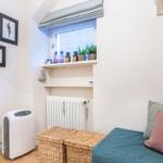 Raum mit Bett, Körben, Heizung und Fenster mit Pflanzen und Flaschen.