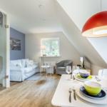 Dining room with table set for four, red pendant light, and view into living area with sofa and window.