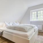 Schlafzimmer mit weißem Bett, Fenster und Holzboden.
