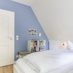 Schlafzimmer mit Bett, Bücherregal und Tür.