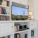 TV on white cabinet with bookshelves and lamp.
