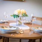 Round wooden table set with plates, glasses, and flower arrangement.