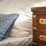 Bed headboard with pillow and wooden chest with two drawers.