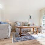 Living room with sofa, coffee table, and windows. Blue rug and wall art.
