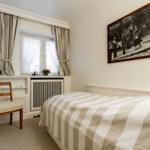 A bedroom with bed, chair, and window. A large photo hangs on the wall.