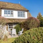 House with thatched roof, white facade, and garden with white chairs.