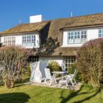 House with thatched roof, white facade, and garden with white outdoor furniture.