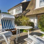 Terrace with lounge chairs and beach cabana in front of a thatched-roof house.