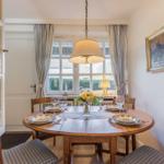 Round wooden table with chairs and table setting in front of window with curtains.