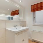 Bathroom with sink, mirror, and window with orange roller blind.