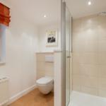 Bath with shower, toilet, and window with orange roller blind.