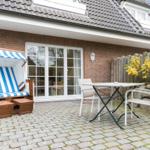 Terrace with beach chair, table and chairs in front of a house with brick wall.