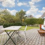 Terrace with table, chairs, and beach chair. Background: greenery and sky.