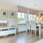 Living and dining area with TV, table and chairs, windows and wooden floor.
