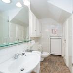 Badezimmer mit Dusche, Waschbecken und Toilette. Weiße Fliesen und Holzboden.