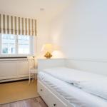 Schlafzimmer mit weißem Bett, Kleiderschrank und Fenster mit Markise.