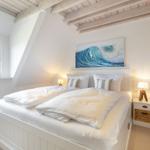 Schlafzimmer mit Doppelbett, Wandbild und Holzbalken an der Decke.