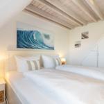 Schlafzimmer mit Doppelbett, Wandbild und Holzbalkendecke.