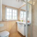 Badezimmer mit Dusche, Waschbecken und Toilette. Fenster mit Blick nach draußen.