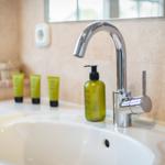 Waschbecken mit Chromhahn und grünen Pflegeprodukten auf Marmorwand