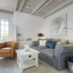 Wohnzimmer mit grauem Sofa, braunem Sessel und Holzbalkendecke.