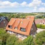 Haus mit rotem Ziegeldach und umliegenden Bäumen unter blauem Himmel.