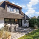 House with thatched roof, terrace with table, chairs, and lounge chair.
