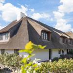 House with thatched roof, windows, and garden under blue sky.