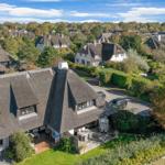 Village with thatched houses and green gardens under blue sky.