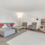 Living room with sofa, armchairs, and TV on white walls.