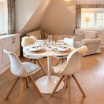 Dining room with round table, white chairs, and windows. Wooden floor and light furnishings.