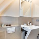 Bathroom with sink, mirror, and shower area under sloped ceiling.