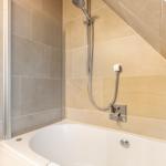 Shower with shower head and bathtub under sloped ceiling