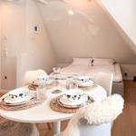 Round table with dishes, white chairs, and sleeping area under gable roof.