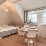 Bedroom with double bed and dining table with four chairs. Wooden floor and large windows.