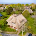 Cottage with thatched roof and green garden. View of the sea.
