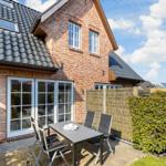 Red brick house with terrace and garden furniture under blue sky.