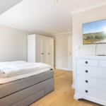 Bedroom with bed, wardrobe, and TV. Wooden floor and white furniture.