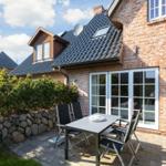 Terrace with table and chairs in front of a house with brick wall and glass doors.