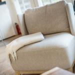 Ein bequemer Sessel mit einer Decke auf dem Sitz. Im Hintergrund ist eine Küche mit Stuhl zu sehen.