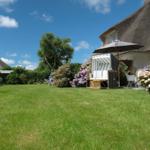 Grüner Garten mit Strandkorb und Sonnenschirm vor einem Haus mit Strohdach.