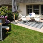 Terrasse mit weißen Stühlen, Tisch und Sonnenschirm neben einem Gartenhaus.