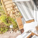 Liegestuhl mit Streifen auf Terrasse neben grüner Hecke.