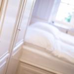 Schlafzimmer mit weißem Bett und Kleiderschrank mit silbernen Knöpfen.