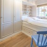 Schlafzimmer mit weißem Bett, Kleiderschrank und blauer Stuhl.
