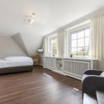 Schlafzimmer mit Bett, Sessel und Fenstern mit Vorhängen.
