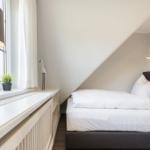 Schlafzimmer mit Dachschräge, Bett und Fensterbank mit Lampe und Pflanze.